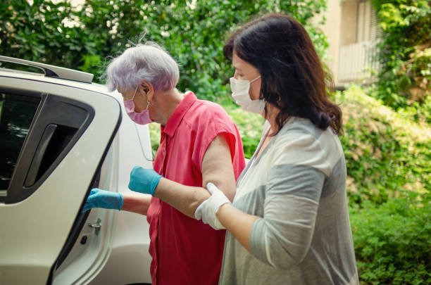 The caregiver goes beyond her normal responsibilities to create a comfortable experience for a senior adult woman during medical appointments. Both wear protective masks.
